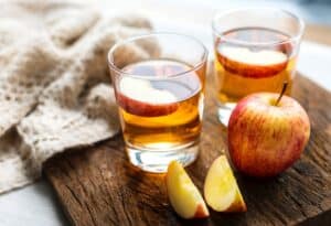 A whole apple and slices next to two cups of apple juice.