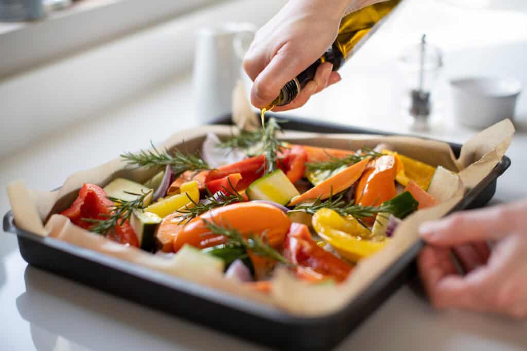 Close Up Of Seasoning Tray Of Vegetables For Roasting With Olive Oil Ready For Vegan Meal